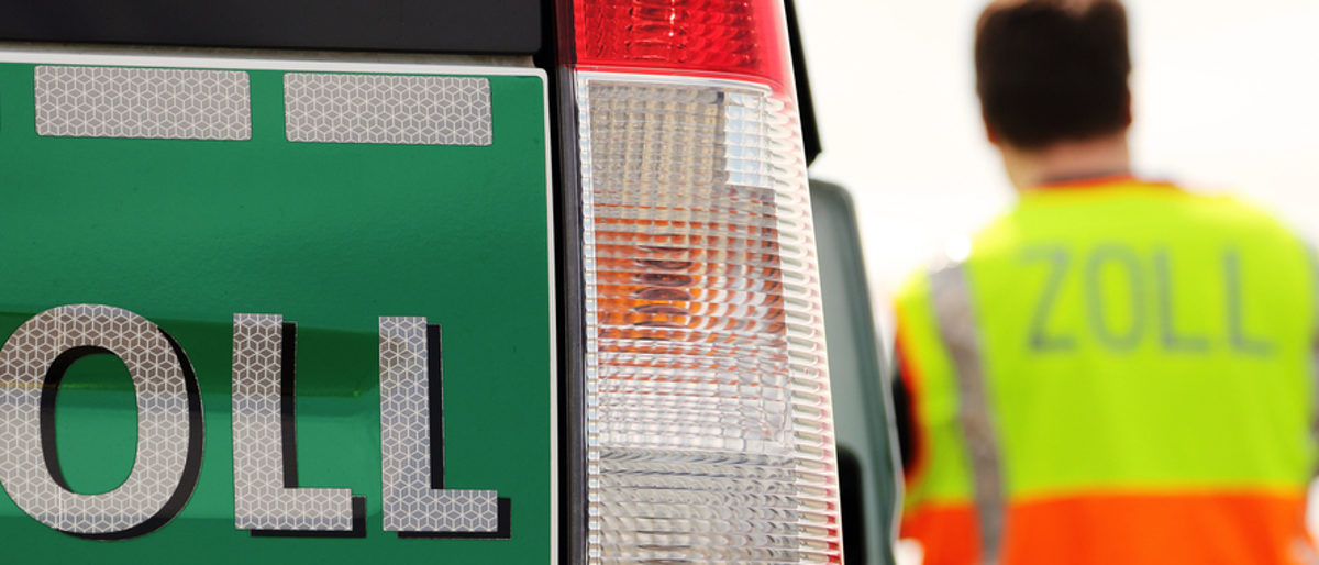 Wer sich auf Schwarzarbeit einlässt, geht ein großes Risiko ein. Vorn im Bild: Heckklappe eines Fahrzeugs mit der Aufschrift "Zoll". Im Hintergrund steht ein Mann mit dem Rücken zur Kamera. Er trägt eine Warnweste, auf der steht auch "Zoll".