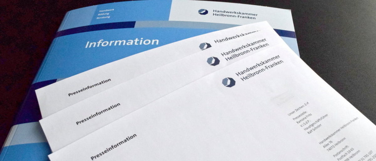 Drei Papierblätter mit der Überschrift Pressemitteilung liegen auf einer hellblauen Mappe, auf der vorne Information steht.