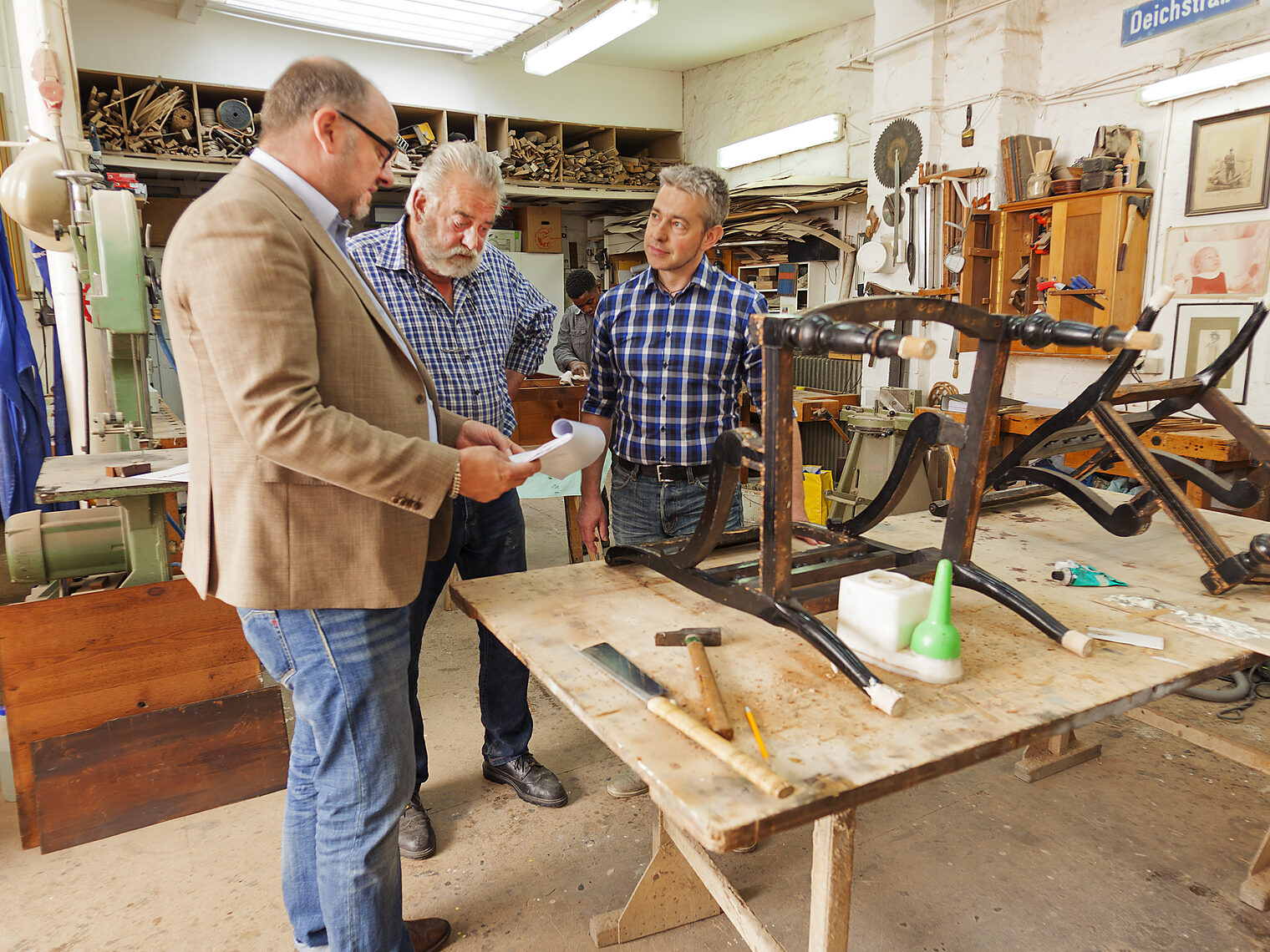 Zwei Handwerker und ein Mann stehen in einer Werkstatt und besprechen etwas
