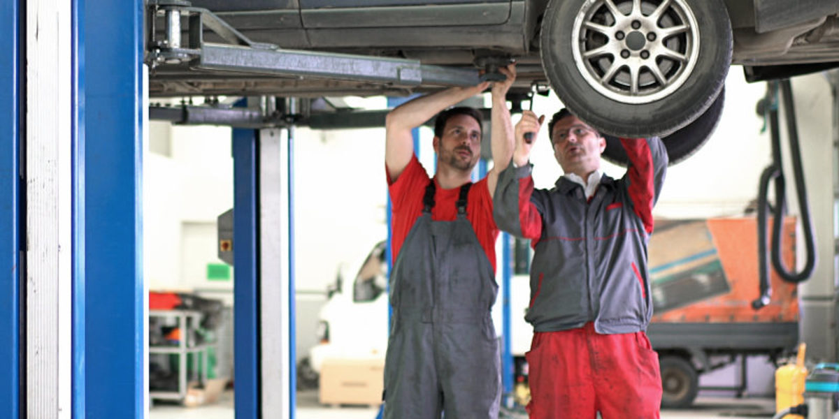 Die Beschäftigung im Handwerk sinkt, zeigt eine aktuelle Umfrage. Zwei Männer in Arbeitskleidung stehen in einer Kfz-Werkstatt. Über ihnen sieht man den Teil eines Autos auf einer Hebebühne.