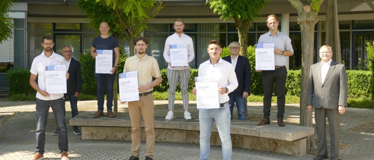 Bereit für den Einsatz als Führungskräfte: die neuen "Geprüften Betriebswirte". Sechs Betriebswirt-Absolventen mit ihrer Urkunde in der Hand stehen vor dem BTZ, dahinter die Prüfer.