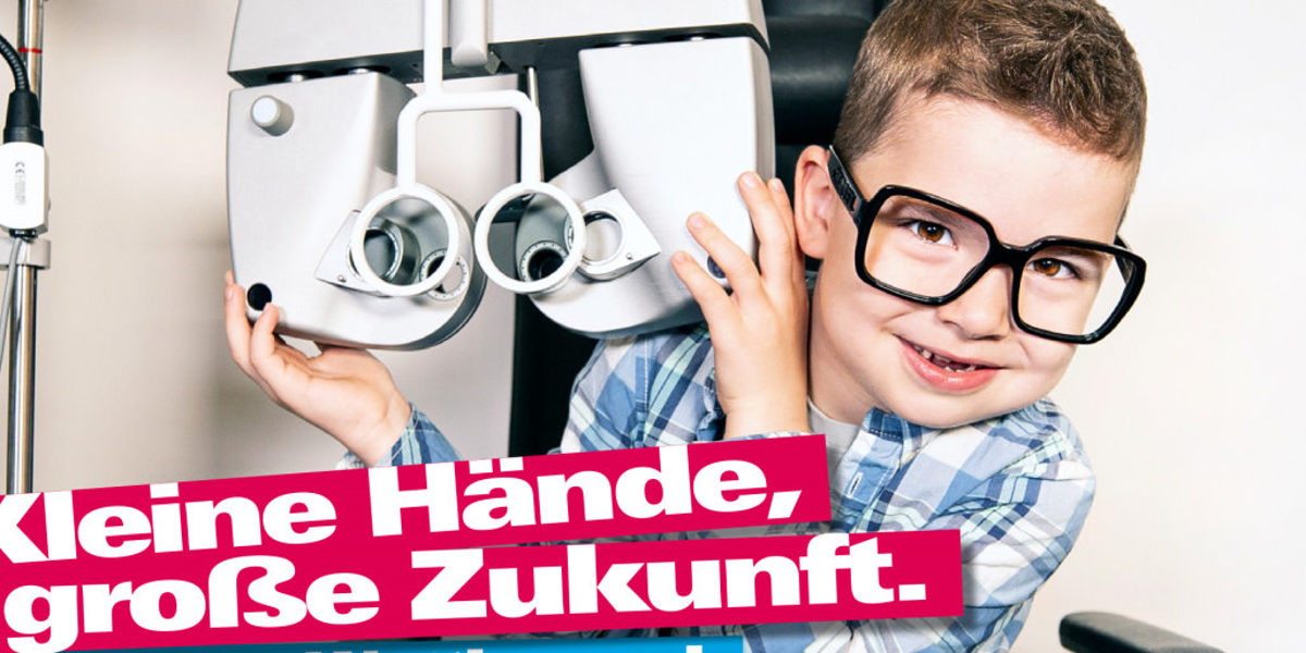 Bundesweiter Kita-Wettbewerb des Handwerks startet wieder. Kleiner Junge mit großer Brille neben einem Sehstärken-Messgerät beim Augenoptiker. Darunter Text Kleine Hände, große Zukunft