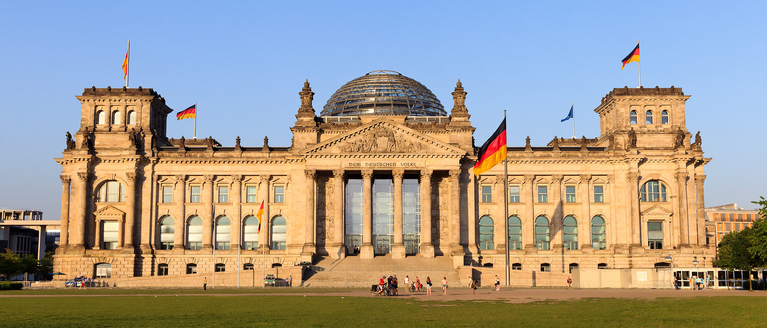 Nach den Koalitionsverhandlungen fordert das Handwerk nun spürbare Maßnahmen. Frontalansicht des Deutschen Reichstags in Berlin mit Deutschlandfahnen und der berühmten Kuppel in der Mitte des Gebäudes.