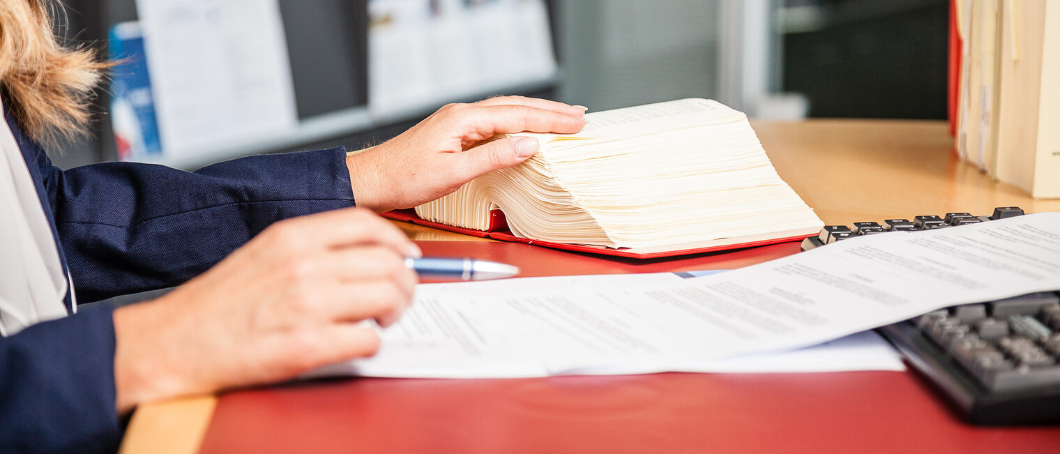 Mitgliedsbetriebe erhalten bei der Handwerkskammer eine Rechtsberatung Eine Frau sitzt an einem Schreibtisch. Vor ihr liegen Dokumente und ein aufgeschlagenes Gesetzbuch.