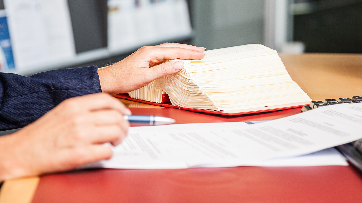 Mitgliedsbetriebe erhalten bei der Handwerkskammer eine Rechtsberatung Eine Frau sitzt an einem Schreibtisch. Vor ihr liegen Dokumente und ein aufgeschlagenes Gesetzbuch.